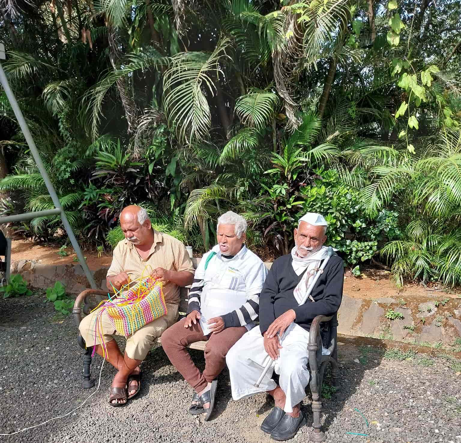 Three residents sitting on a bench, enjoying the nature. One of them is making baskets.